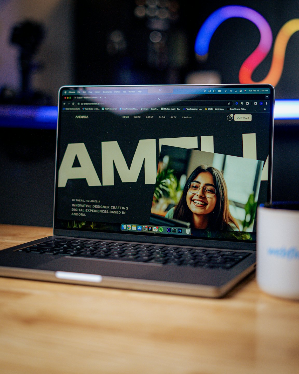 A laptop screen displays a designer portfolio on a wooden desk.